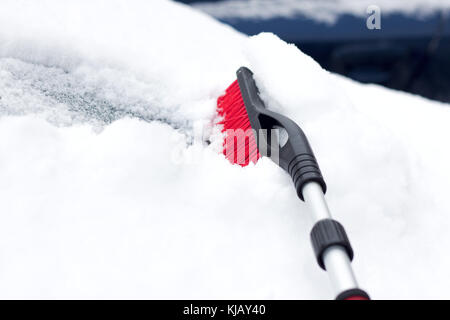 Nevoso inverno in una città in una giornata di sole. auto dopo la nevicata nel parcheggio. giovane donna cercando di aprire il gelido auto . Foto Stock