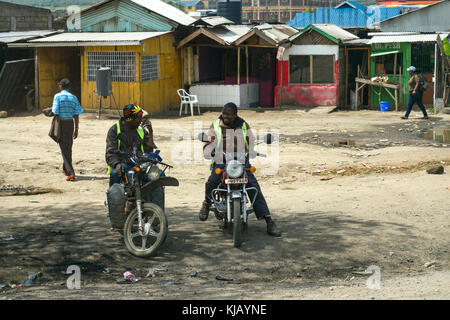 Due uomini africani sedersi a parlare nel loro moto in ombra nella parte anteriore di edifici di fortuna, Kenya, Africa orientale Foto Stock