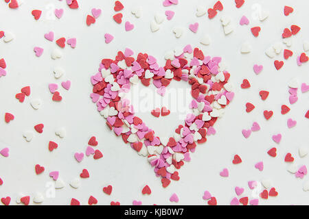 Cuore realizzato da multi-zucchero confettini colorati caramelle sparse sulla pietra bianca. sfondo romantico San Valentino compleanno carità giornata della madre. Messaggio di saluto Foto Stock