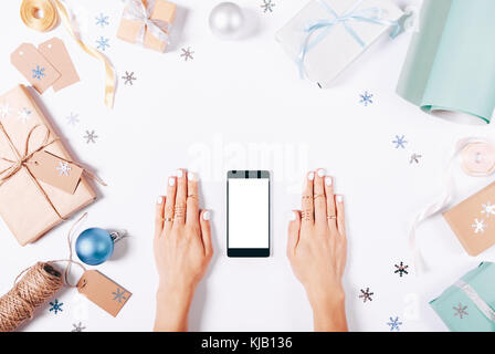 Mani femminili e il telefono cellulare con una schermata vuota su un tavolo bianco tra le decorazioni di Natale Foto Stock