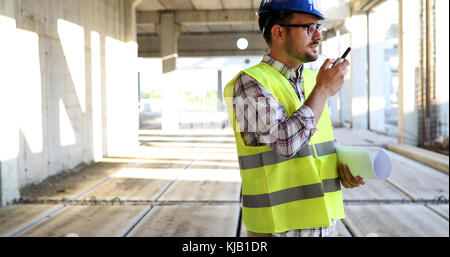 Architetto maschio con blueprint utilizzando un walkie-talkie Foto Stock