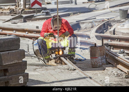 Lavoratore con maschera protettiva di saldatura i binari del tram della città Foto Stock