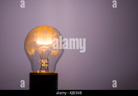 Foto orizzontale con singolo bulbo di vetro. La lampadina è accesa ma il filo è in fiamme. Il fumo colorato di arancione dal fuoco di riempimento di spazio interno. th Foto Stock