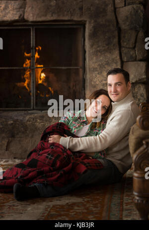 Sorridente coppia caucasica cuddling sul pavimento vicino al camino Foto Stock