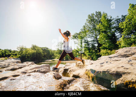 La donna caucasica saltando sulle rocce vicino al fiume Foto Stock