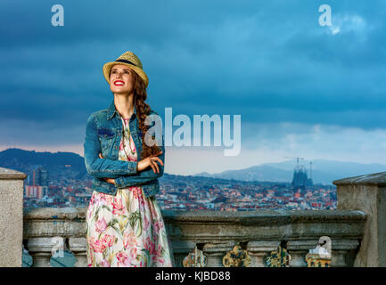 Serata perfetta con vista mozzafiato. Sorridendo eleganti donna in abiti lunghi e cappello di paglia a Barcellona Spagna guardando in lontananza Foto Stock