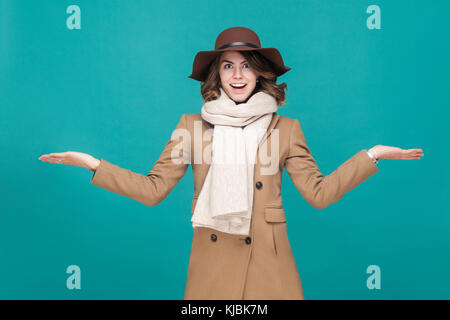 Lo stupore donna vestita di ricoprire, cappello e sciarpa. studio shot, isolato su sfondo blu Foto Stock