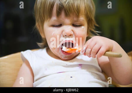 Confuso bambino mangiare con il cucchiaio Foto Stock