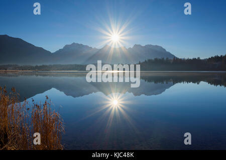Le montagne Karwendel sono retroilluminate dal sole riflesso nel lago di Barmsee a Kruen, nell'alta Baviera, in Germania Foto Stock