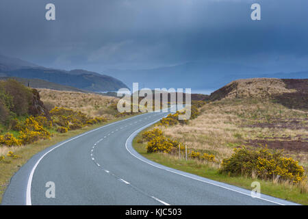 Tortuosa strada di campagna con un cielo sovrastato in primavera sull'isola di Skye in Scozia, Regno Unito Foto Stock