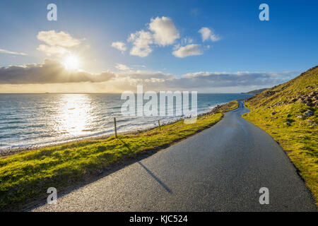 Tipico paesaggio scozzese sull'isola di Skye con una strada costiera e il sole che splende sull'oceano, Scozia, Regno Unito Foto Stock