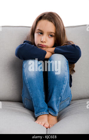 Poco ragazza seduta su un divano e sconvolto con qualcosa Foto Stock