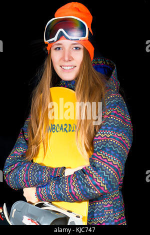 Ragazza bionda con capelli lunghi con lo snowboard e abbigliamento sportivo invernale in studio. Foto Stock