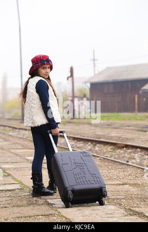 Bambina con una valigia, in piedi presso la stazione in attesa di un treno  Foto stock - Alamy