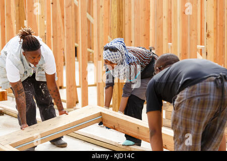 I volontari di sollevamento del telaio in legno al sito in costruzione Foto Stock