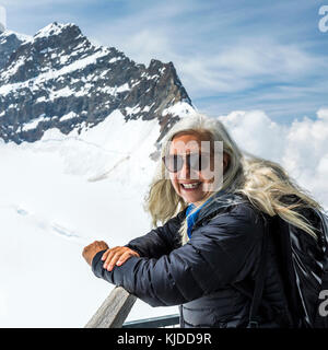 Ritratto di sorridente donna caucasica appoggiata sulla ringhiera vicino montagne Foto Stock