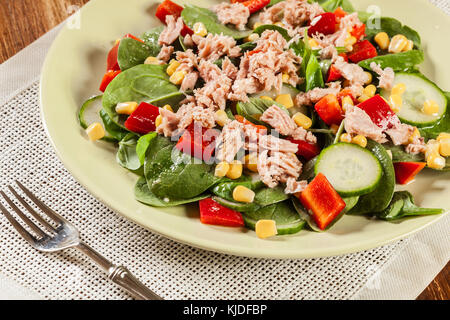 Spinaci freschi con insalata di tonno, cetriolo, mais e la paprica rossa su una piastra. Un sano cibo crudo concetto. Foto Stock