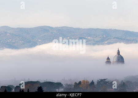 Splendida vista su Santa Maria degli Angeli chiesa papale (Assisi) metà coperti dalla nebbia all'alba Foto Stock