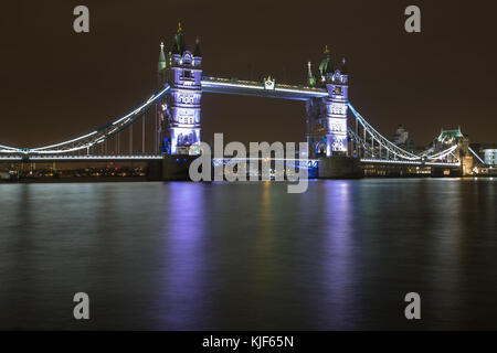 Il Tower Bridge sul fiume Tamigi di notte illuminato in viola con la riflessione in acqua - Londra, Regno Unito Foto Stock