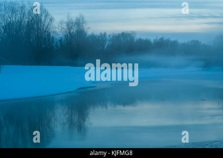 Paesaggio notturno con il fiume, parzialmente coperti di ghiaccio, neve sulla riva e la nebbia sull'acqua, Shot con esposizione lunga Foto Stock