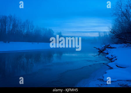 Paesaggio notturno con il fiume, parzialmente coperti di ghiaccio, neve sulla riva e la nebbia sull'acqua, Shot con esposizione lunga Foto Stock
