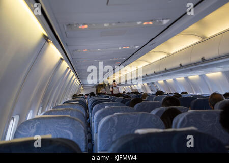 La cabina di un aereo con Airhostess dicendo avviso di sicurezza, come si vede dal retro del piano Foto Stock