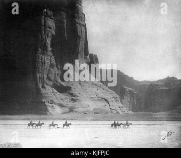 Fotografia di un gruppo di nativi americani che cavalcano cavalli nel deserto, di fronte al Canyon de Chelly, intitolata "Canyon de Chelly (pronuncia De Shay)", di Edward S Curtis, Arizona, 1904. Dalla New York Public Library. Foto Stock