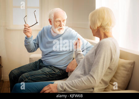 Grave uomo barbuto sollevando i suoi occhiali Foto Stock