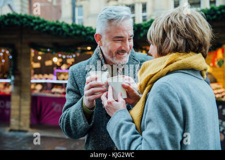 Coppia matura sono bere bevande calde in una città mercato di Natale. Essi sono la tostatura le tazze monouso. Foto Stock
