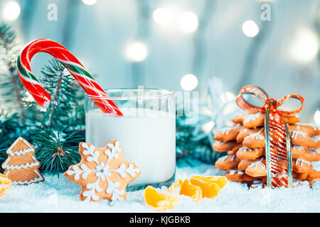 Natale pan di zenzero e latte con decorazioni, neve, albero di natale succursali sul bokeh sfocato sullo sfondo delle luci. spazio libero Foto Stock