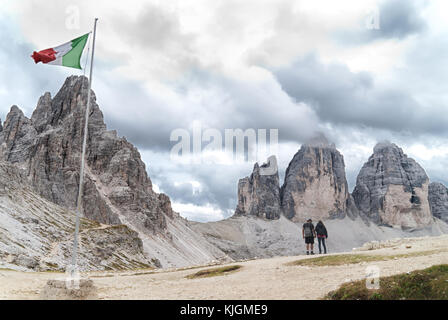 Bandiera italiana e due escursionisti in parte anteriore del Monte Paterno (paternkofel) e cloud-coperto tre cime di Lavaredo nelle Dolomiti Foto Stock