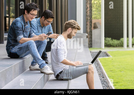 Gruppo di asian multietnica e la gente di affari con abito casual lavora con ogni tecnologia di attrezzature con felice azione al pubblico esterno, persone Foto Stock