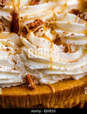 Godere di ringraziamento con un grafico a torta di zucca cheesecake. cheesecake è coperto con la panna montata e le noci pecan, poi spruzzato con sciroppo di caramello. Foto Stock