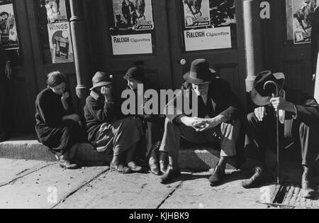 Una fotografia di tre donne e due uomini seduti su un palco di cemento all'esterno di un edificio, i due uomini indossano entrambi cappelli e abbigliamento formale, le tre donne indossano tutti abiti e maglioni, sono stati riuniti con altre persone nell'ambito di un incontro religioso, sei manifesti pubblicitari sigarette sono fissati all'esterno dell'edificio dietro di loro, Tennessee, 1935. Dalla New York Public Library. Foto Stock