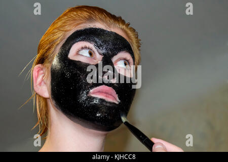 La ragazza di un cosmetico maschera nera. Maschera di pulizia di aspirina e carbonio attivato. cosmetico nero maschera facciale Foto Stock