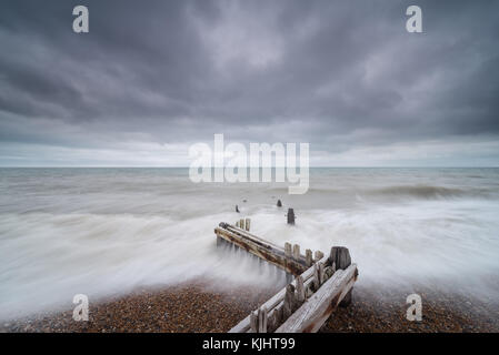 Legno stagionato groyne a Rye Harbour con mare rotondo a cascata. Foto Stock