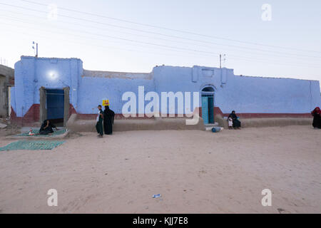 Gli abitanti di un villaggio di appendere intorno al crepuscolo al di fuori del loro tradizionale blu nubian case in un piccolo villaggio sulle rive del fiume Nilo in Aswan, Sud Egitto. Foto Stock