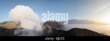 Dalla cresta del bromo del cratere interno, un panorama mostra i fumi solforico, gunung batok picco e un mare di nuvole che corrono sul cratere interna Plain Foto Stock