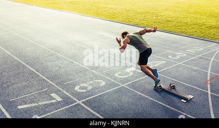 Vista posteriore di un atleta di iniziare il suo sprint su un all-weather via di corsa. Runner con blocco di partenza per iniziare la sua esecuzione sulla pista. Foto Stock