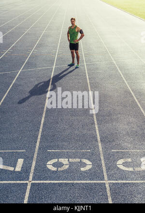 Runner permanente sulla via di corsa con le mani piegate. Atleta che indossa auricolari con telefono mobile fissato nella fascia braccio. Foto Stock