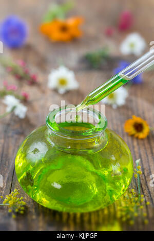 Trasparente bottiglie in vetro con gocce di liquido essenziale in contagocce su sfondo di legno con fiori di medicinali Foto Stock
