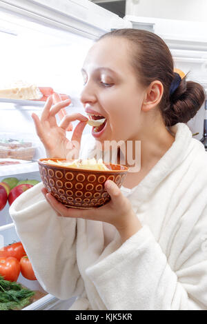 Divertimento giovane donna mangiare patatine all'interno del frigorifero Foto Stock