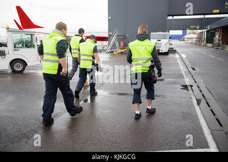 Lunghezza piena vista posteriore dei lavoratori di sesso maschile a piedi su pista bagnata Foto Stock