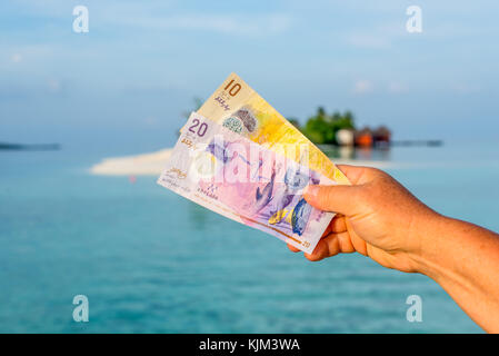 Un turista lo spettacolo della rupia maldiviana bank nota quando si viaggia in Maldive. Il denaro delle Maldive bank nota nella femmina la mano sullo sfondo della isl Foto Stock