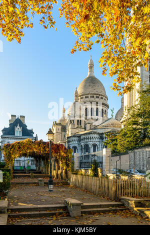 Vista posteriore della Basilica del Sacro Cuore di Parigi in autunno a sunrise visto da un parco pubblico con foglie di colore arancione contro il cielo blu. Foto Stock