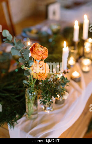 Presente, sera cena concetto. close up incredibile di grandi gemme di luce delicata orange roses, posizionato come mazzetto in vaso trasparente sul bianco seta drapping Foto Stock