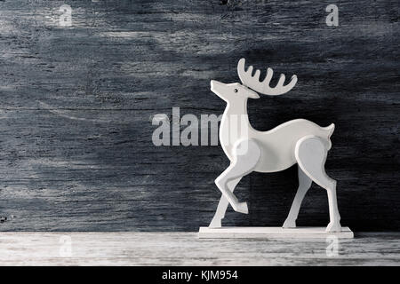 Un bianco di renne di legno contro un rustico grigio superficie di legno con un bianco spazio vuoto sulla sinistra Foto Stock