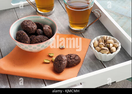 Rustico con biscotti al cioccolato e noci in tazza di ceramica, servito sul vassoio in legno con due tazze di tè e un bicchiere di fresco di pistacchi Foto Stock