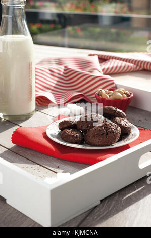 Rustico cacao Biscotti e pistacchi sul vassoio in legno con una bottiglia di latte, zuccheriera alluminio, pistacchi freschi, cubetti di zucchero e tovaglia con striping Foto Stock