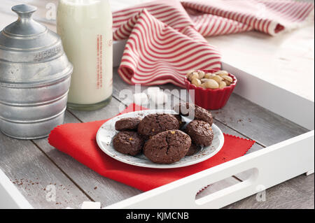 Rustico cacao Biscotti e pistacchi sul vassoio in legno con una bottiglia di latte, zuccheriera alluminio, pistacchi freschi, cubetti di zucchero e tovaglia con striping Foto Stock